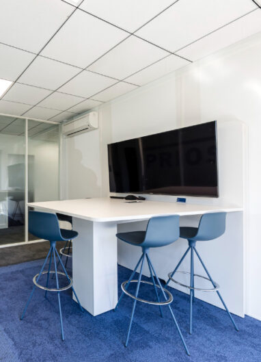 un espace visioconférence avec une table haute des tabourets et un écran au mur