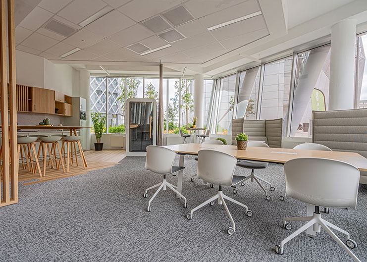 un espace de travail avec au premier plan une table avec des sièges à roulettes, des alcoves acoustiques et au second plan une cabine phone box