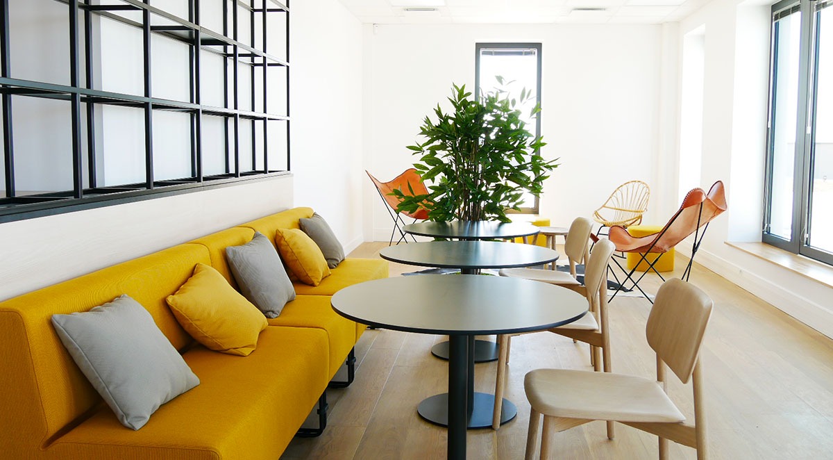 Un espace cafétéria; canapé jaune; des tables et sièges