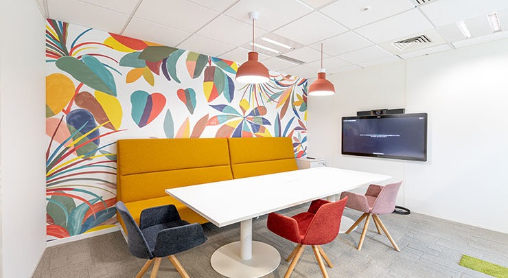 un espace bureau avec une tapisserie colorée en fond un fauteuil orange, une table et un écran de télévision