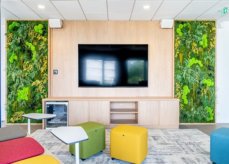un espace de bureau ouvert avec un mur végétalisé un écran de tv et des poufs colorés