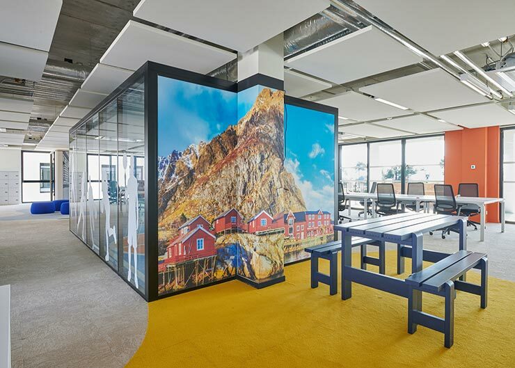 un espace de travail ouvert avec une table et des bancs en bois et au fond un papier peint avec un paysage de Norvège