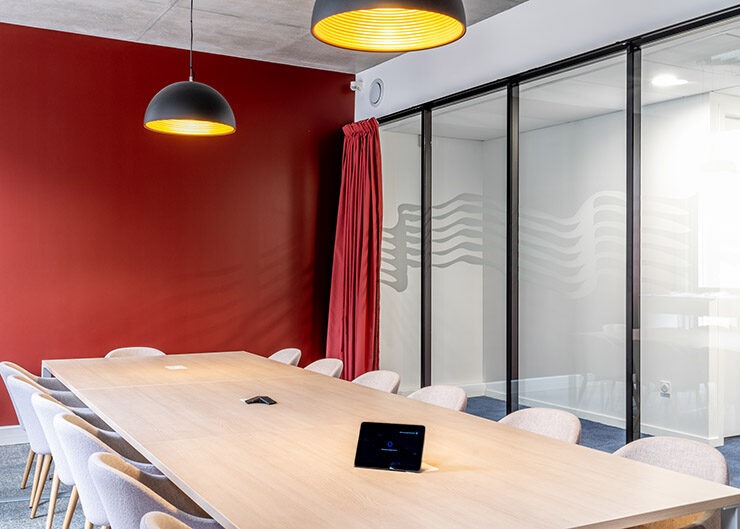Une salle de réunion collaborative avec un mur peint en rouge au fond, une grande table et des sièges