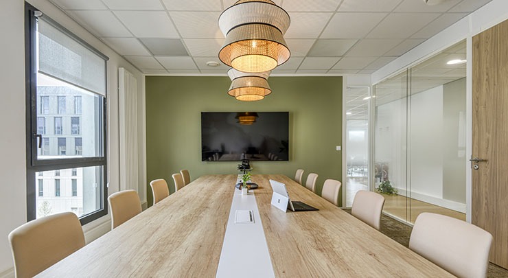 un espace collaboration réunion avec une grande table un écran tv mural sur un mur vert