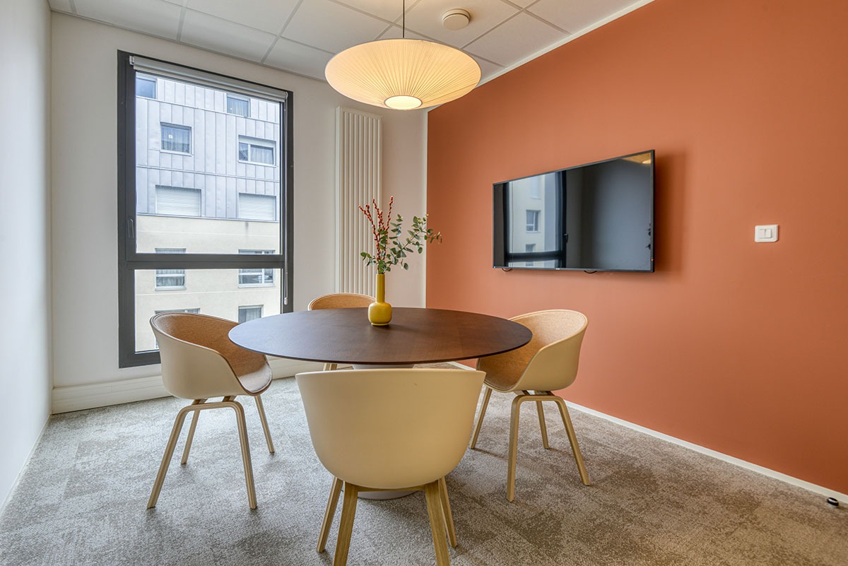 Un espace réunion avec une table ronde , des sièges et un écran tv sur mur orange