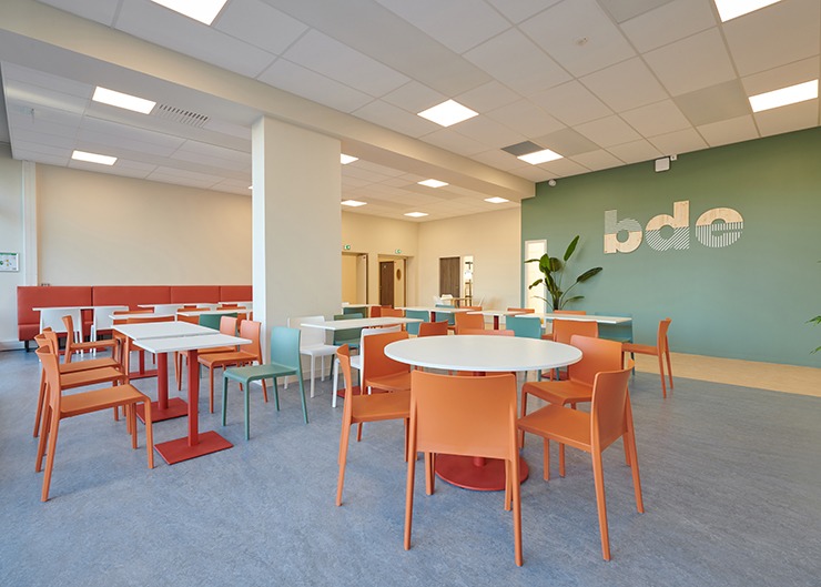 Un espace cafeteria avec des tables et chaises orange et un mur vert au fond