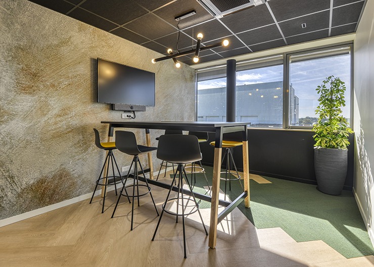 un espace de travail collaboratif avec une table haute un écran de télé au mur habillé d'un papier peint