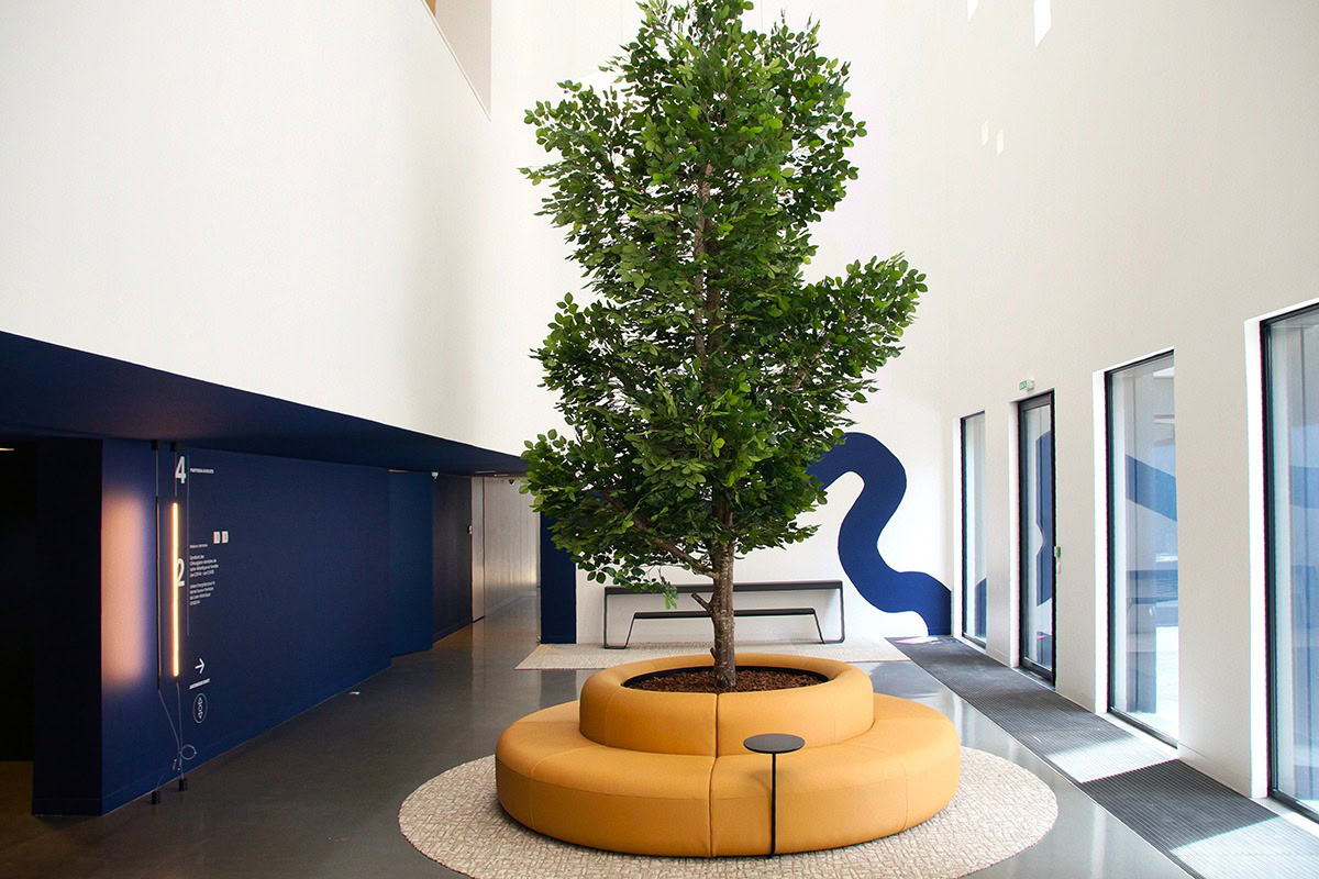 Un grand hall d'immeuble avec un canapé circulaire et un arbre au centre
